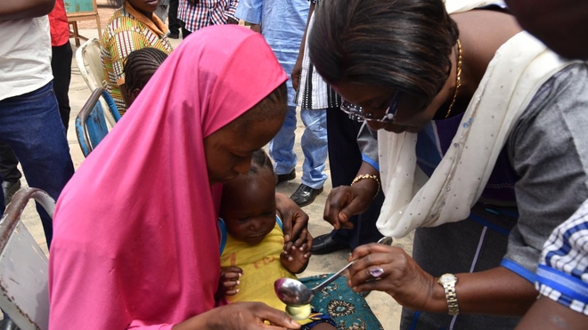 Le Représentant de l’OMS au Burkina Faso, Dr Alimata J. DIARRA-NAMA aidant une mère à administrer une dose de médicament de chimio prévention du paludisme à son enfant